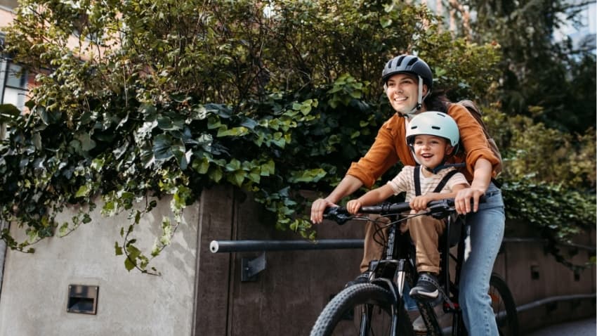 Eine Mutter fährt mit ihrem Sohn lachend zusammen auf einem Fahrrad.